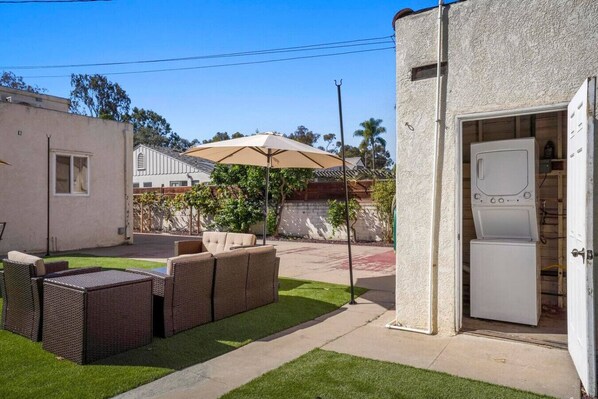 A backyard with a patio set, a lawn, and a utility room with a washing machine.