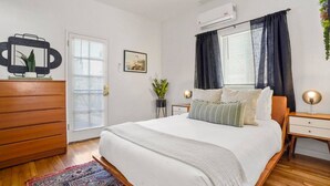 A bedroom with a bed, dresser, bedside tables, an air conditioner, and a window with curtains.