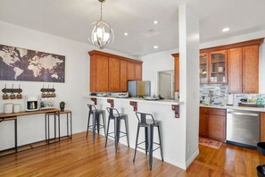 Uma cozinha moderna com armários de madeira, um espaço de bar com banquetas, um mapa-múndi na parede e uma luminária pendente.