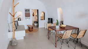 A modern interior with a dining area, white sofas, a wooden tree sculpture, and a TV. - Grand Cave Villa with Outdoor Hot Tub (Thira - Santorini)