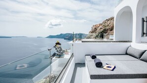 A balcony with a view of the sea, a seating area with cushions, and a potted plant. - Grand Cave Villa with Outdoor Hot Tub (Thira - Santorini)