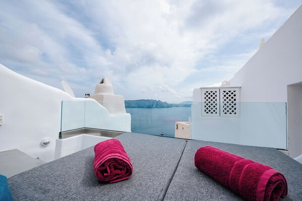 A modern hotel room with a view of the sea, a grey textured table, and two rolled towels.