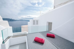 A balcony with a clear view of the sea, white walls, and two rolled towels.