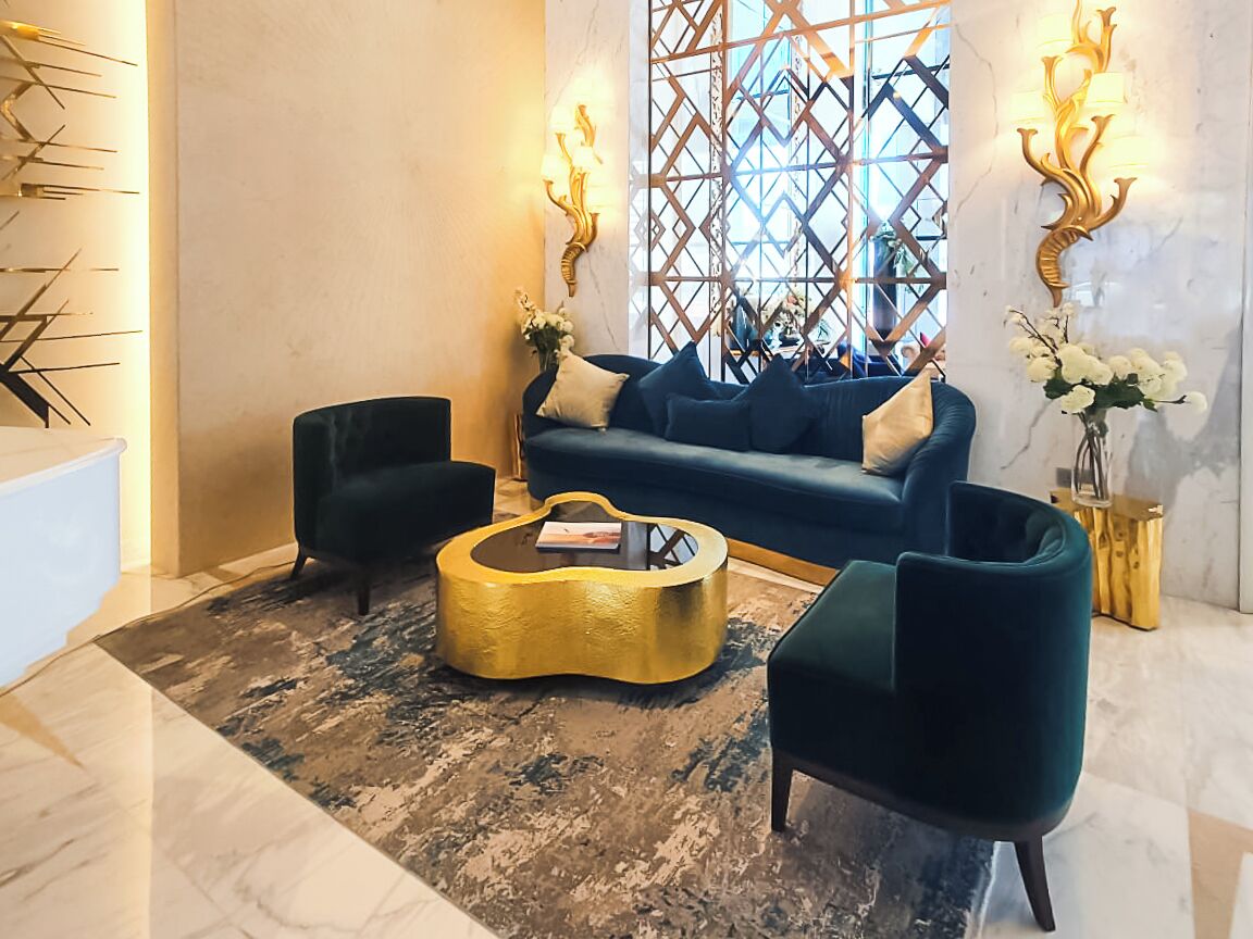 Eine moderne Lobby mit einem blauen Sofa, zwei Sesseln, einem goldenen Couchtisch und dekorativen Wandleuchten.