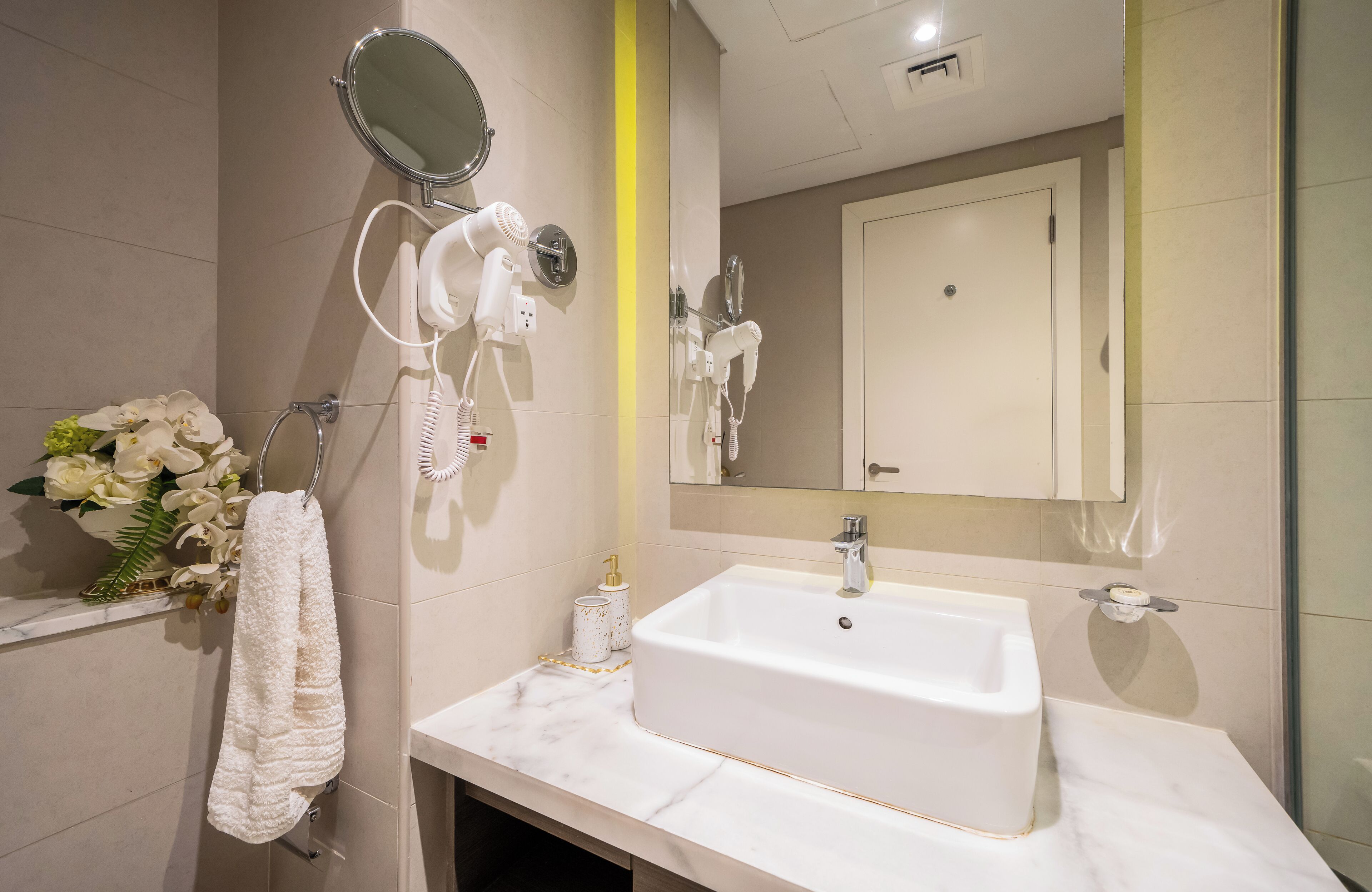 Ein modernes Badezimmer mit einem weißen Waschbecken, einem Spiegel und einem an der Wand befestigten Föhn.