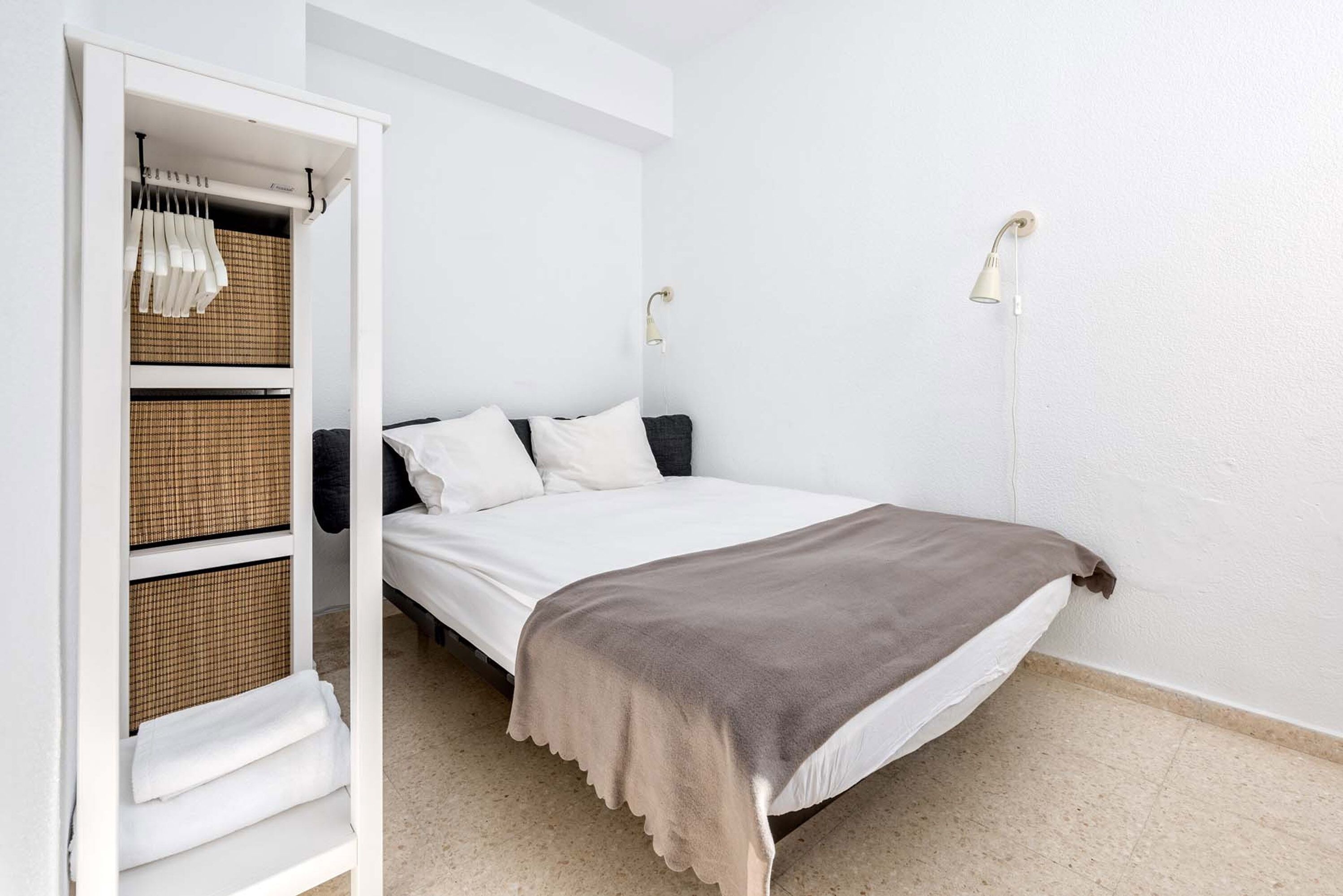Un dormitorio con una cama, un armario blanco y dos lámparas de pared.