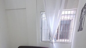 Et værelse med flisegulv, en lilla sofa, et spisebord med en stol og et vindue med hvide gardiner.