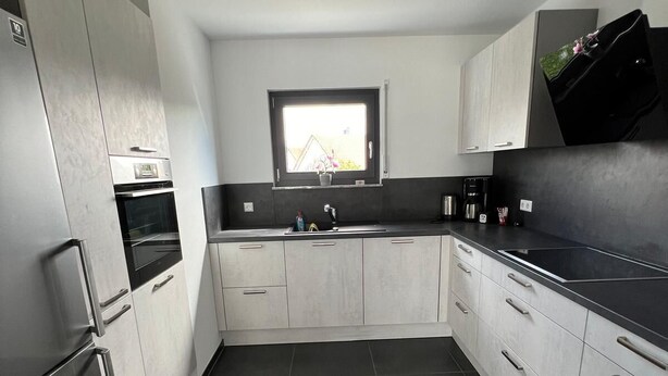 Una cocina moderna con armarios blancos, encimera negra y una ventana sobre el fregadero.