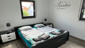 Un dormitorio moderno con una cama grande, dos mesitas de noche, una ventana y un adorno en la pared.