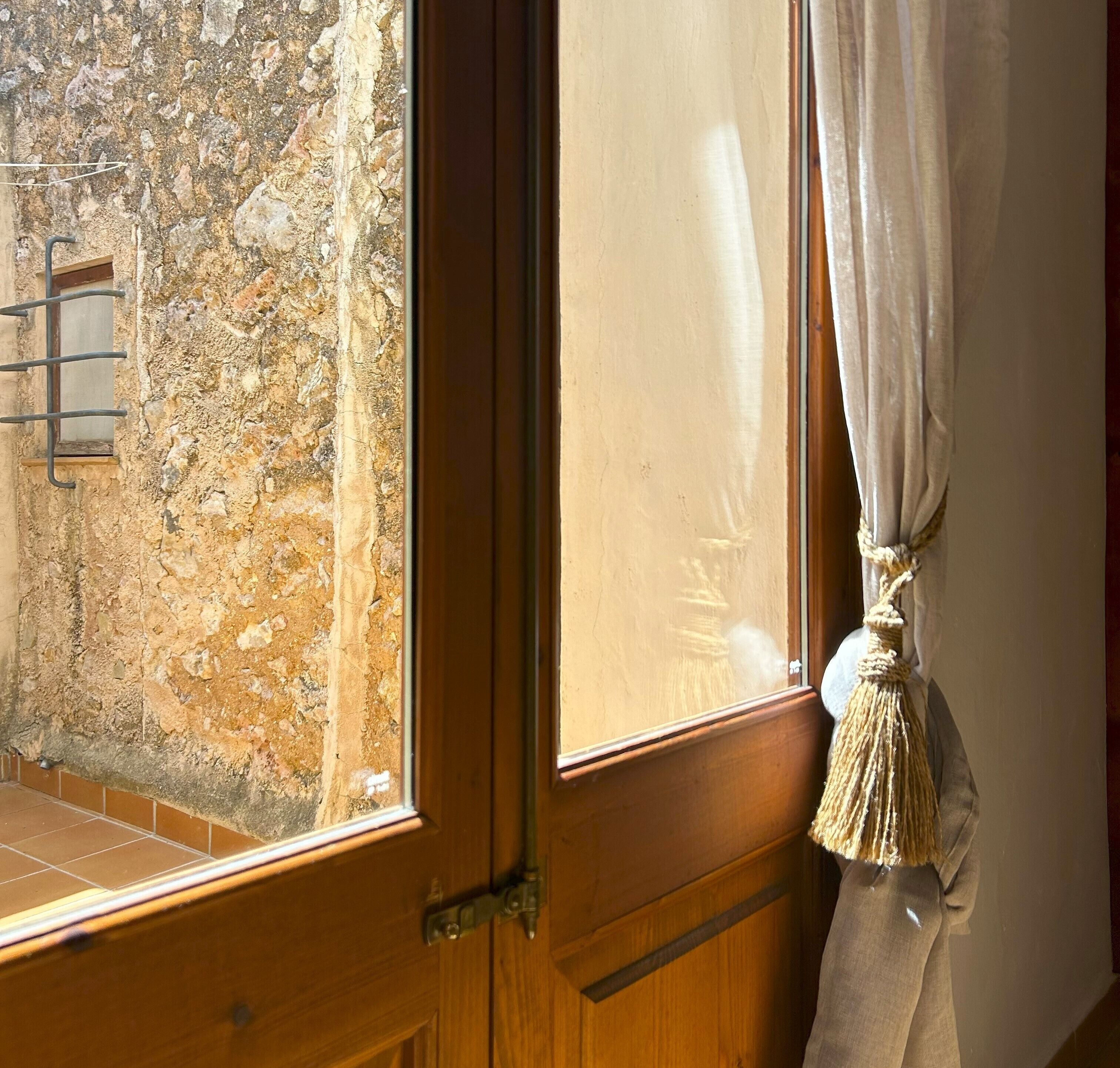 A wooden door with a window, a stone wall, and a curtain tied with a tassel.
