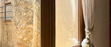 A wooden door with a window, a stone wall, and a curtain tied with a tassel.