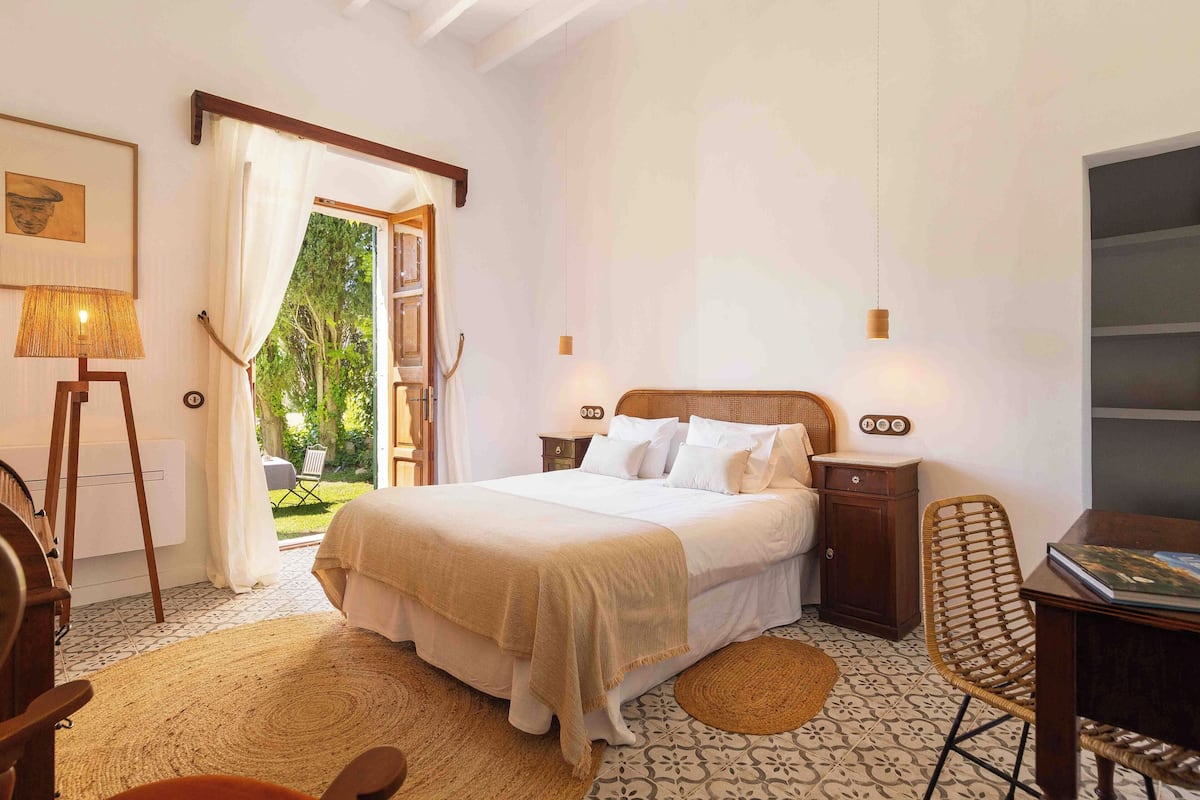 A bedroom with a bed, bedside tables, a chair, a desk, and a view of the outdoors.