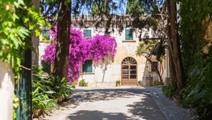 A cobblestone street leading to a building with a wooden door and a window with green shutters. - Fangar Agroturismo (Campanet)
