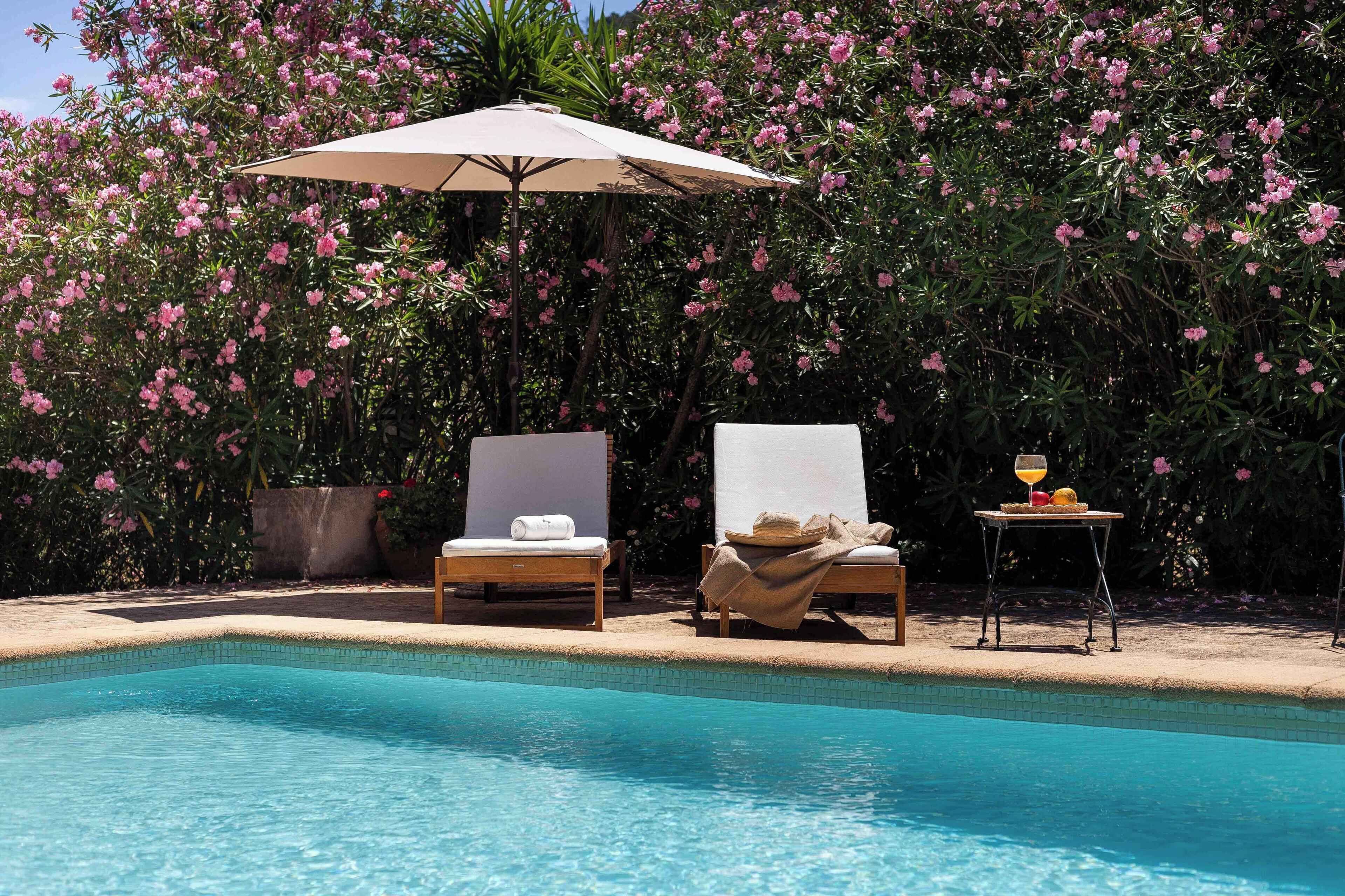 A poolside area with two lounge chairs, a table with a drink, and an umbrella.
