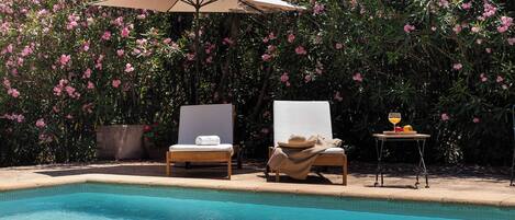 A poolside area with two lounge chairs, a table with a drink, and an umbrella.