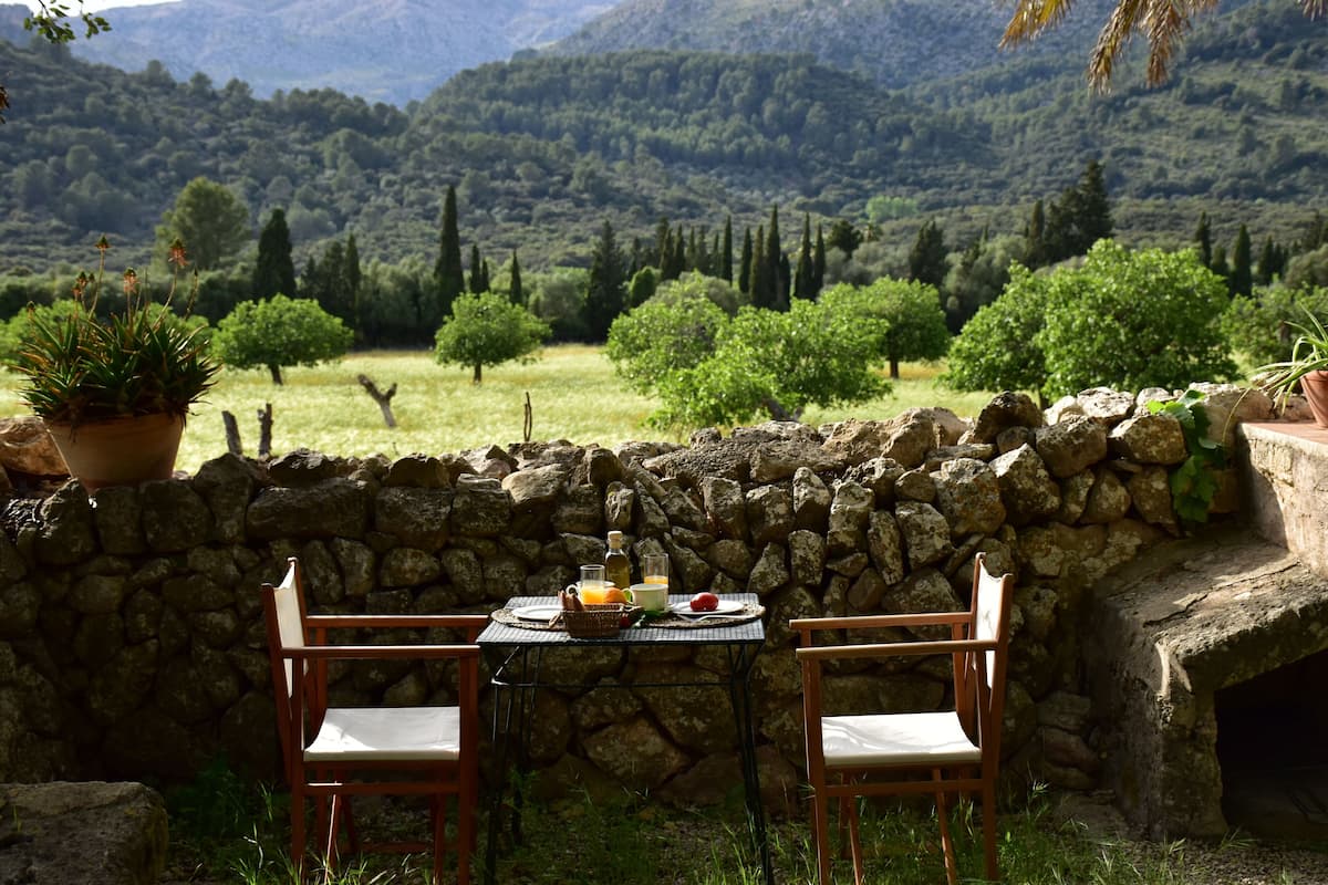 A stone wall with a table and chairs in a garden setting, overlooking a lush valley.