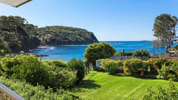 A coastal view with a grassy lawn, trees, and a clear blue sea. - Waterfront Home with Bay Views | Sprindrift (Malua Bay)