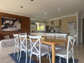 A modern kitchen with white cabinets, a wooden dining table, and white chairs. - Waterfront Home with Bay Views | Sprindrift (Malua Bay)