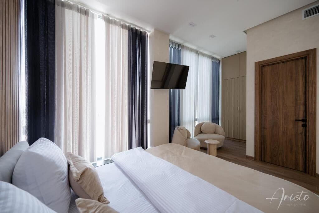 A modern hotel room with a large bed, a TV mounted on the wall, and a wooden door.