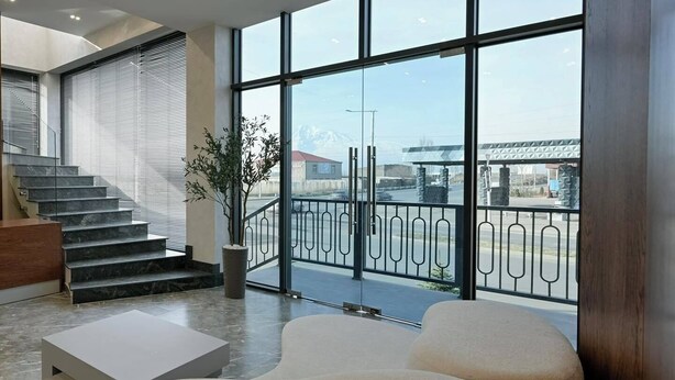 A modern hotel lobby with a staircase, a seating area, and large windows offering a view of the city. - Aristo (Artashat)