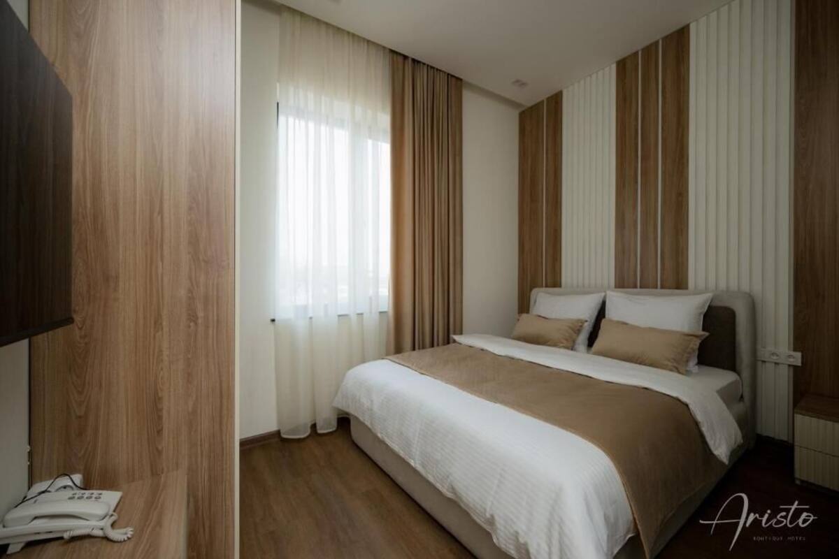 Ein Hotelzimmer mit Bett, Vorhängen, Telefon und Holzvertäfelung.