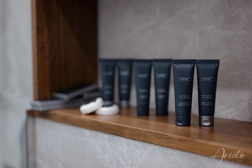 Une étagère sur laquelle se trouvent plusieurs flacons de produits de toilette de couleur foncée, portant les étiquettes « Aristo » et « Lotion pour le corps », le tout posé sur une surface en bois.
