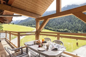 Eine Holzdar Terrasse mit einem für das Frühstück gedeckten Tisch mit Blick auf eine gebirgige Landschaft.