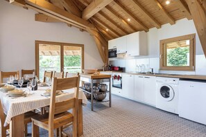 Une cuisine avec des poutres en bois, des meubles blancs, une table à manger dressée avec des assiettes et des verres, et un lave-linge.