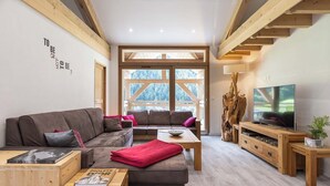 A cozy living room with a sofa, coffee table, TV, and wooden beams. - Résidence Chalet Les Amis (Peisey-Nancroix)