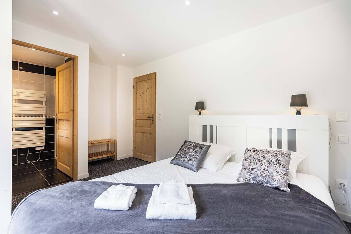 A bedroom with a bed, two bedside lamps, a wooden wardrobe, and a bench.