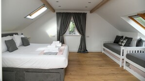 Een slaapkamer met een groot bed, een kleiner bed, een raam met gordijnen en een dakvenster.