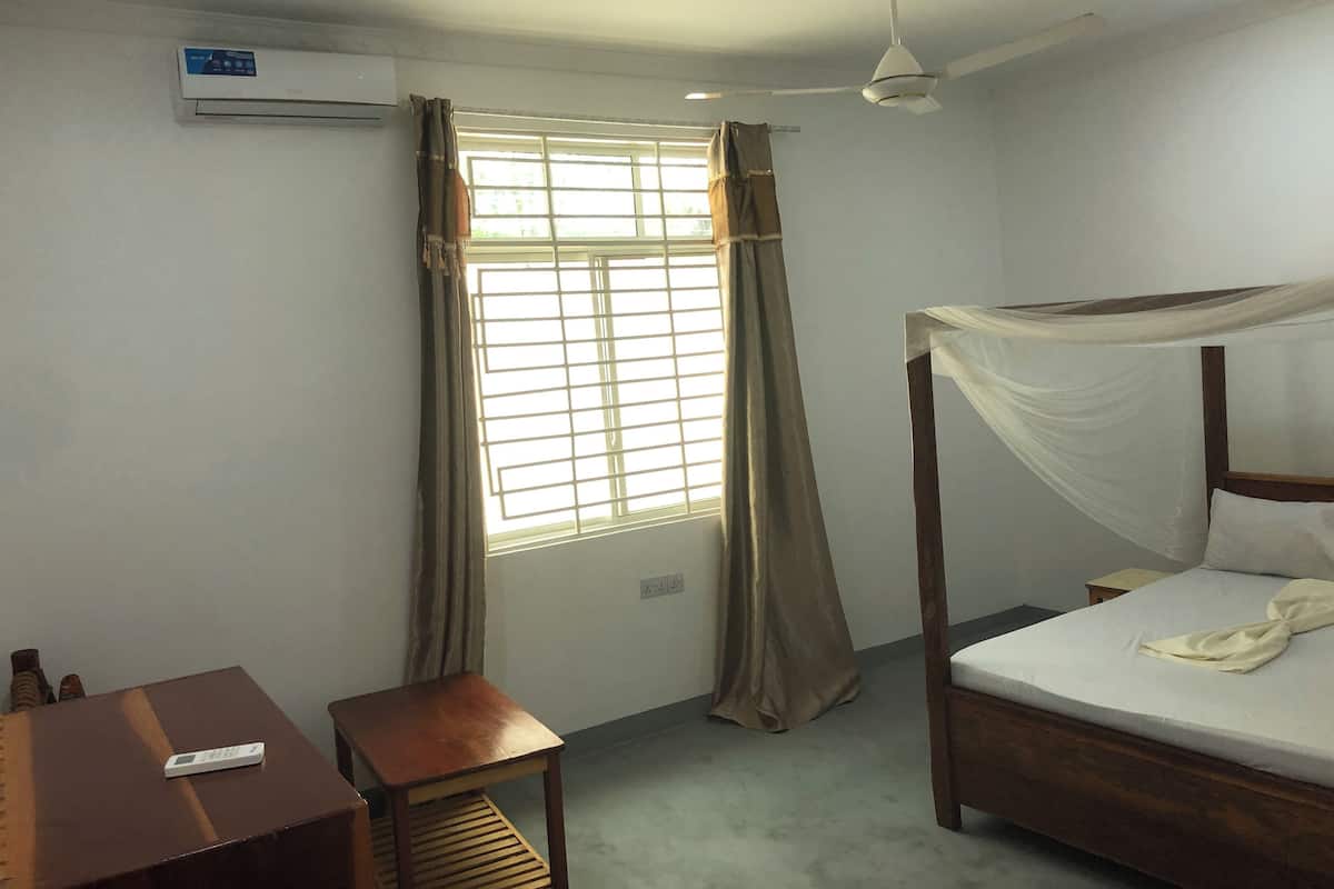 A bedroom with a bed, a desk, a chair, a ceiling fan, and a window with curtains.
