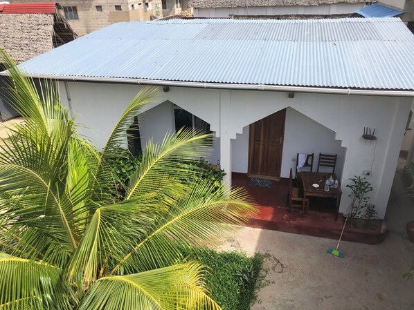 A two-story building with a corrugated metal roof, a wooden door, and a small outdoor seating area with a table and chairs. - Misonobarini Sweet Villa (Nungwi)