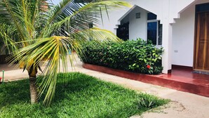 A modern building with a white exterior, a red-tiled entrance, and a well-maintained garden with a palm tree and shrubs. - Misonobarini Sweet Villa (Nungwi)