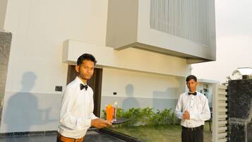 Two individuals standing outside a building with a modern design, a tiled floor, and a small garden area.