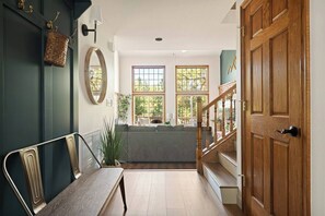 Un pasillo con un banco, una puerta de madera, una escalera y vistas a un balcón con plantas.