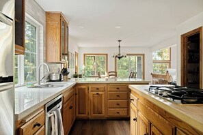 Una cocina con armarios de madera, una isla central, una estufa empotrada y ventanas grandes.