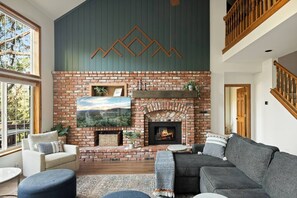 Una sala de estar con chimenea de ladrillo, un televisor montado y un sofá.