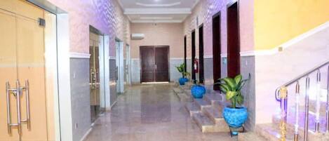 A hotel corridor with a marble floor, glass doors, and potted plants.