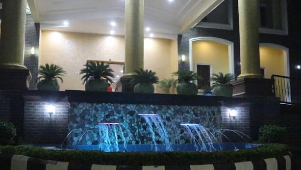 A night-time fountain with water jets, surrounded by potted plants and a stone wall. - Vertex- View Hotel and Suites  (Awka)