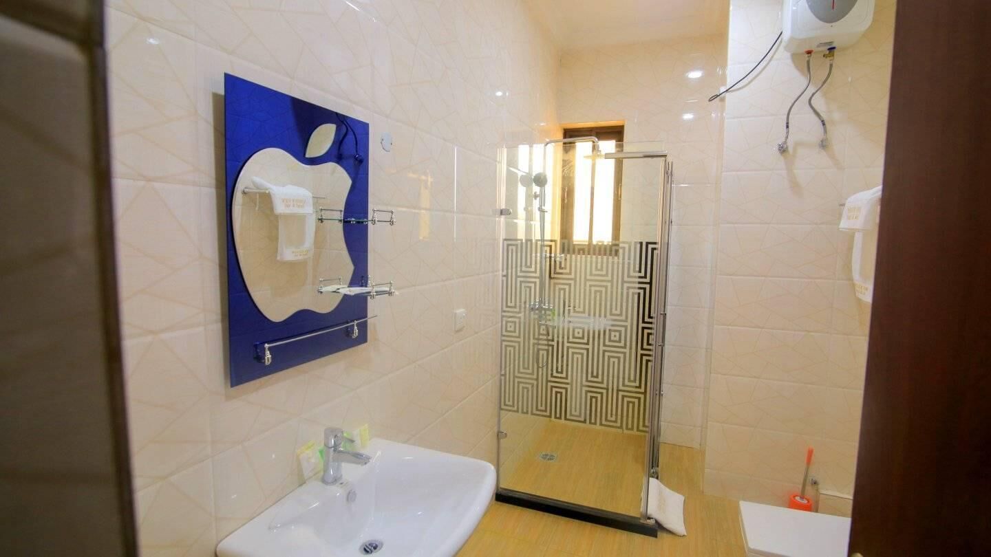 Un baño con un lavamanos blanco, un espejo azul con el logotipo de Apple, un box de ducha de cristal y una puerta de ducha con motivos decorativos.