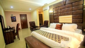 A hotel room with a large bed, two chairs, a small table, and a desk. - Vertex- View Hotel and Suites  (Awka)