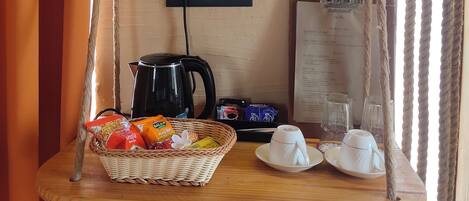 A room with a swing chair, a basket of snacks, a kettle, and a menu on the wall.