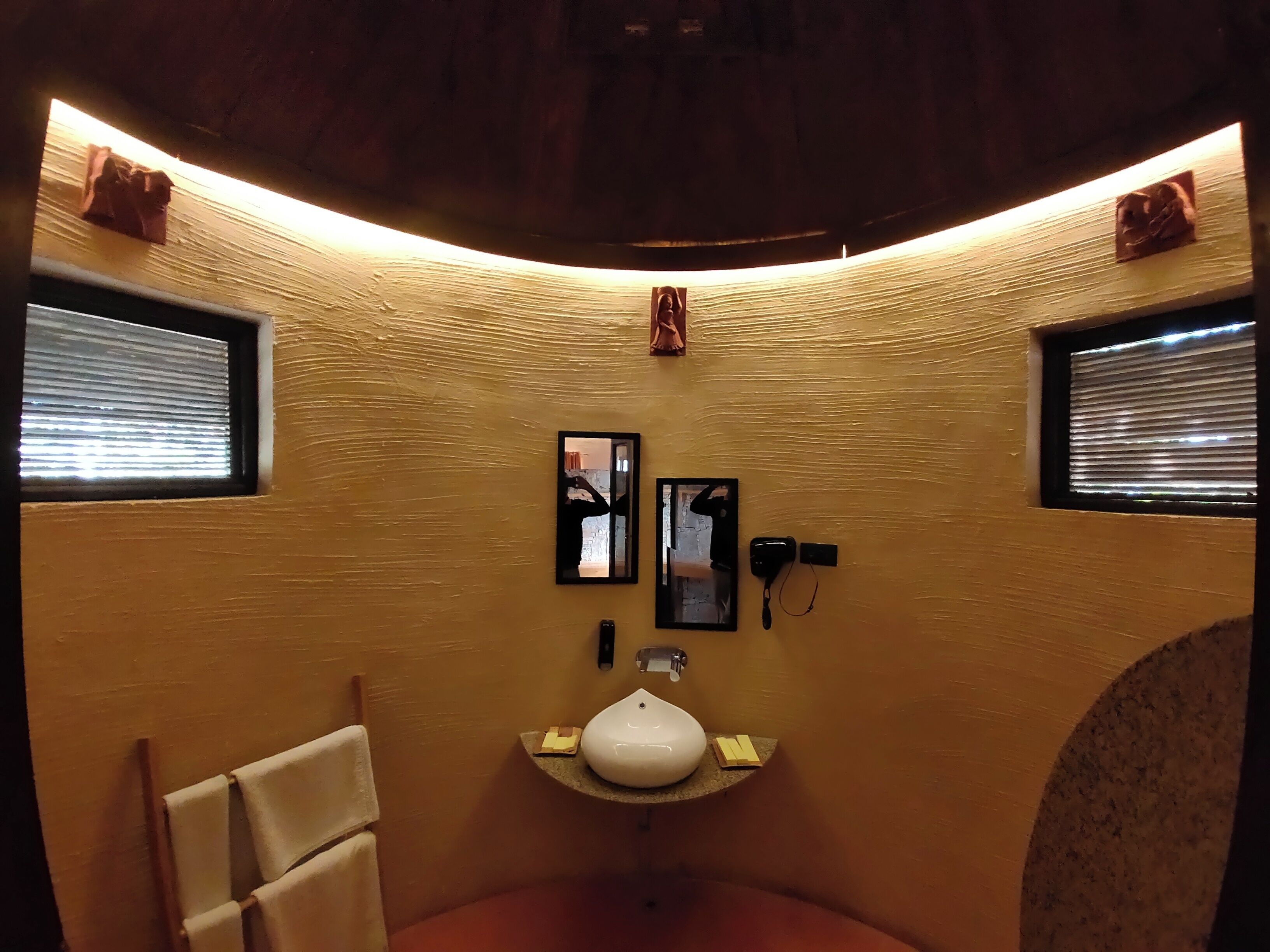 A small, curved bathroom with a single sink, a mirror, and two windows.