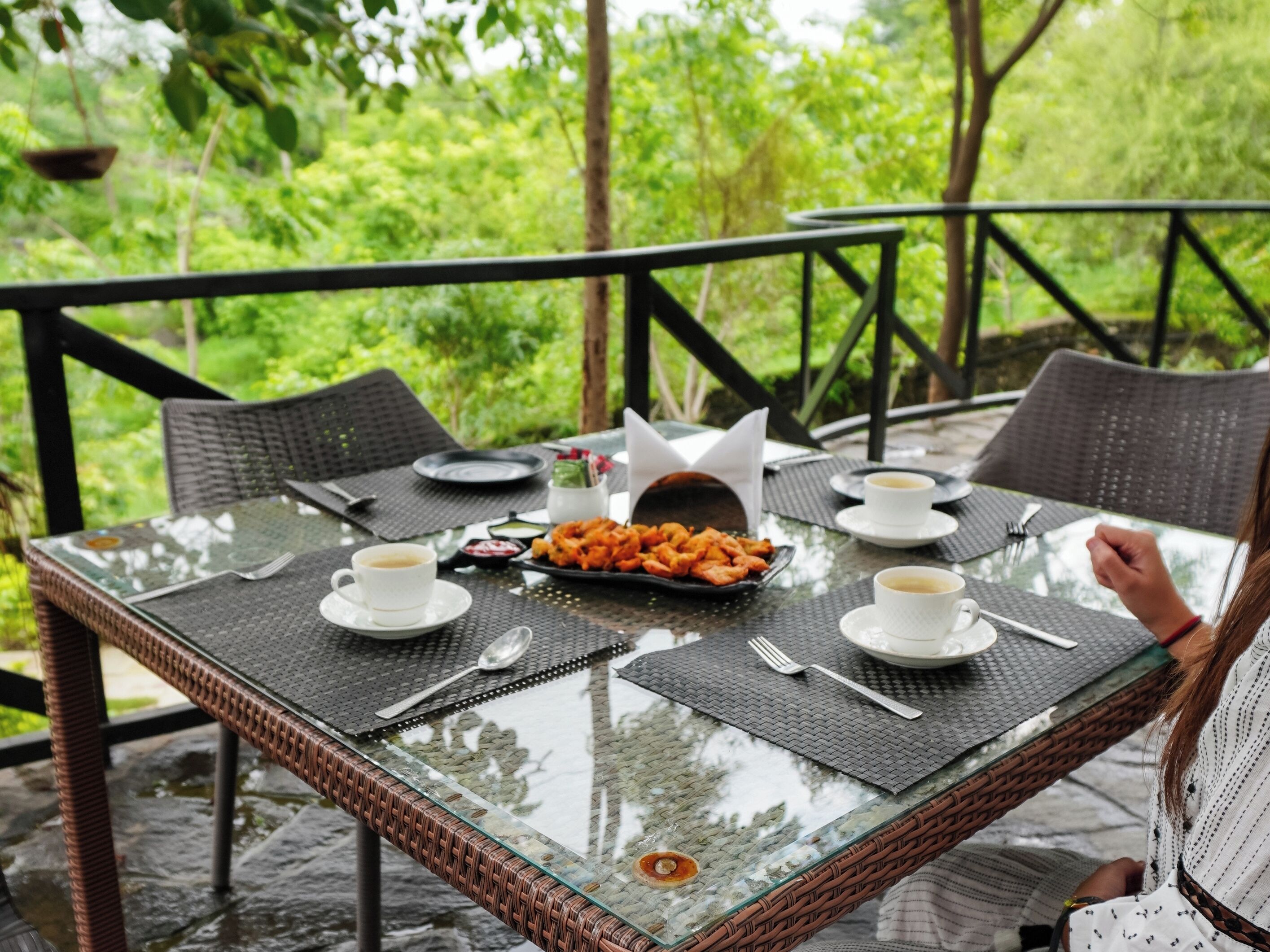 Une table à plateau en verre, dotée d'un cadre en osier, entourée de chaises, posée sur un sol en pierre et offrant une vue sur une végétation luxuriante.