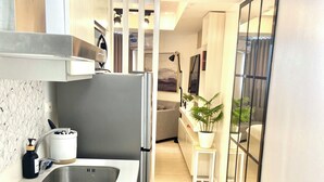 A modern kitchen with a built-in stove, a stainless steel sink, and a refrigerator. There is a small island with a sink and a potted plant. The kitchen leads to a living area with a sofa and a coffee table. - Cozy studio in beautiful San Fernando with AC, WiFi and Pet Friendly  (San Fernando)