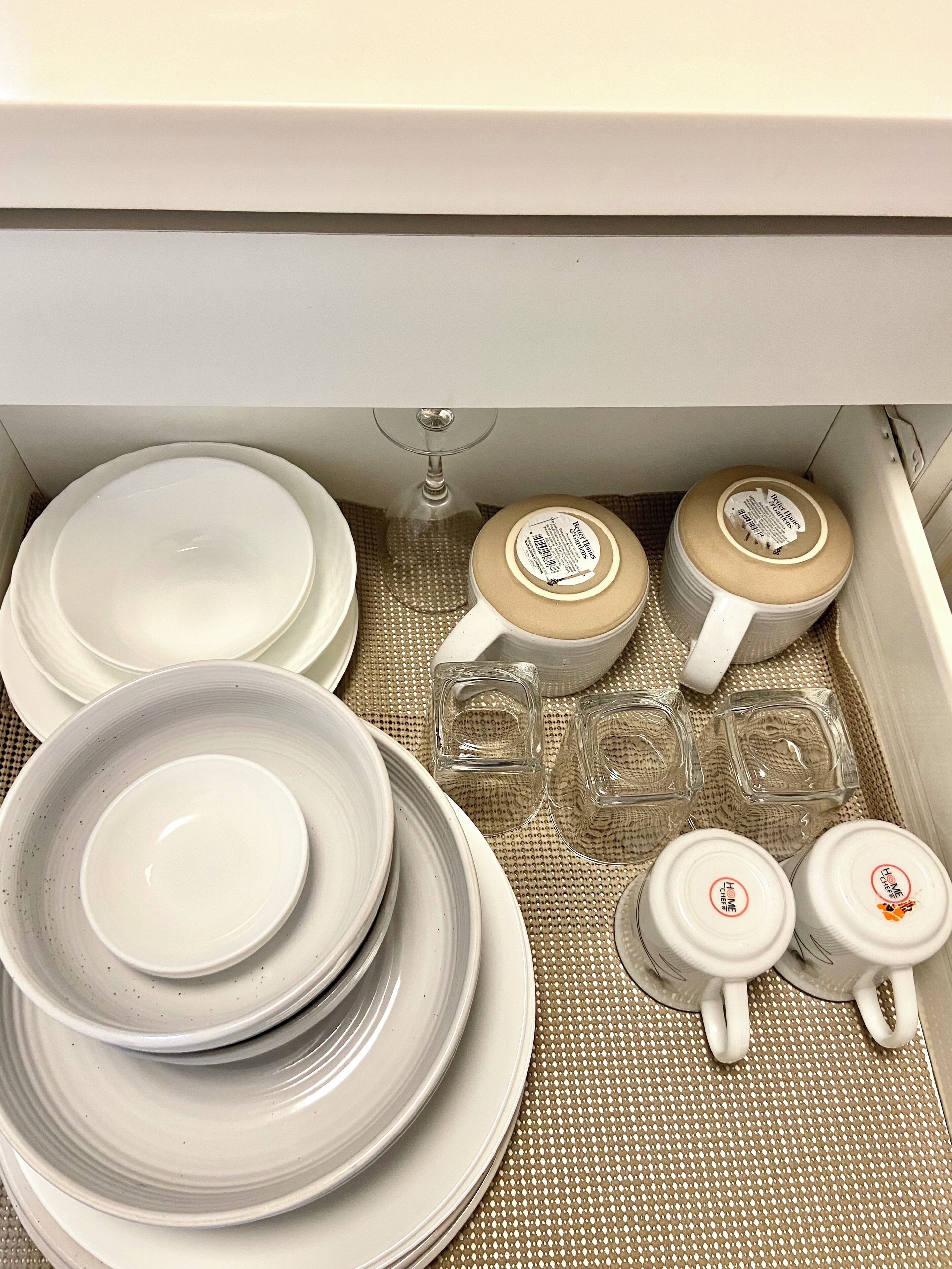 A storage area with white plates, bowls, and glassware neatly arranged on a woven mat.