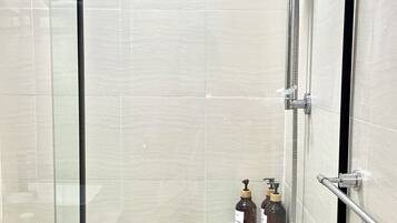 A glass-enclosed shower stall with a handheld showerhead, a handheld shower attachment, and a white bucket.