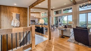 A spacious living area with a wooden staircase, a dining area, and large windows offering a view of the outdoors. - Berry Refined - Luxury, views, hot tub, spacious (Morganton)
