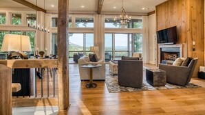 A spacious living area with a fireplace, large windows, and a wooden interior. - Berry Refined - Luxury, views, hot tub, spacious (Morganton)